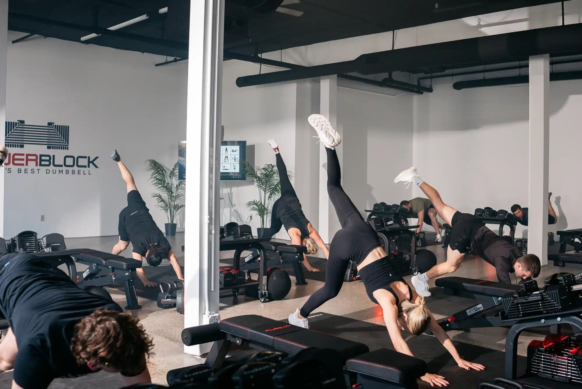 multiple strength training members stretching during a trainer led class at a boutique PowerBlock fitness studio