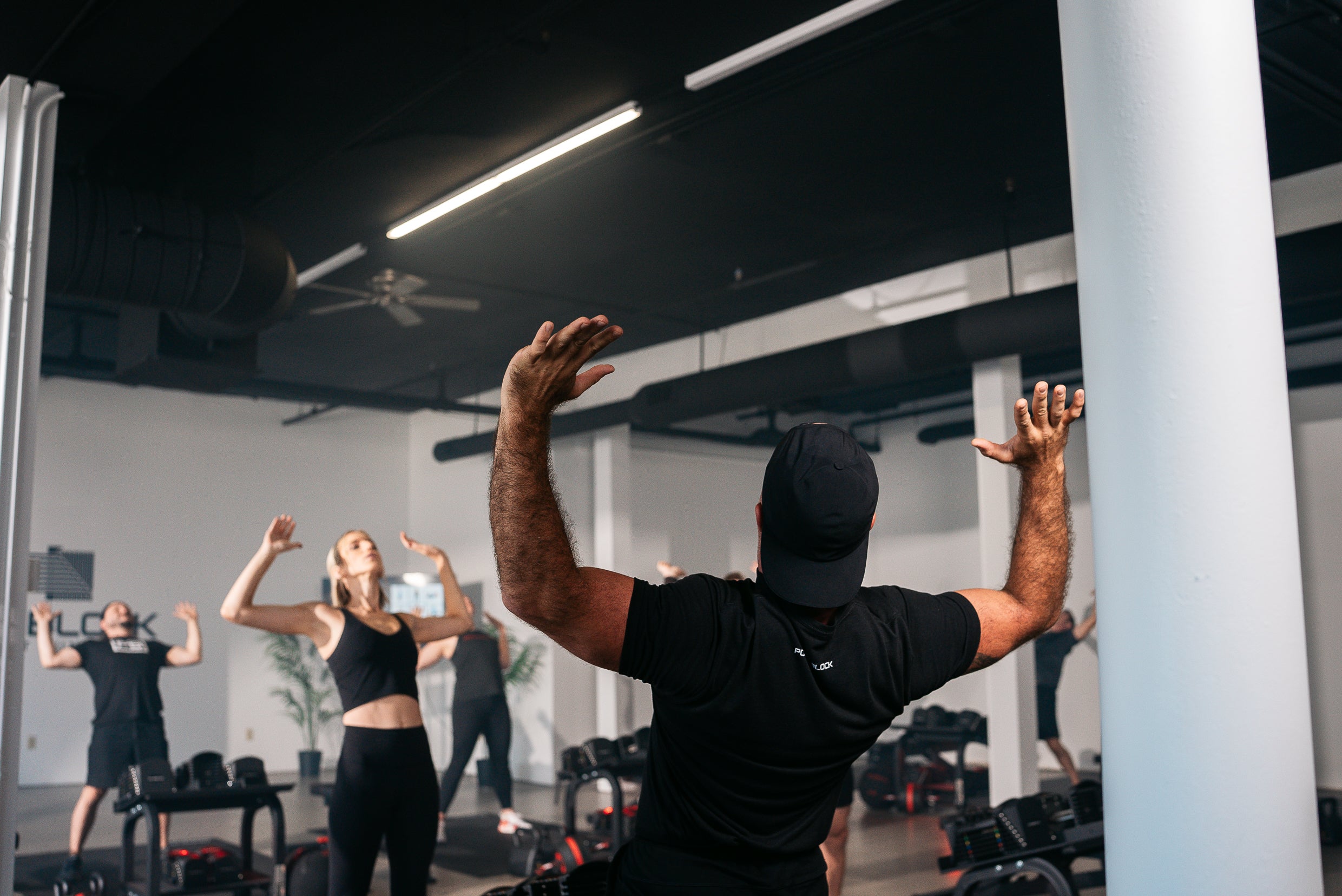 A powerblock fitness studio coach going through a stretch with members, in a hiit based class format.
