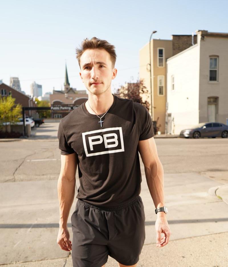 PowerBlock fitness studio's Coach Joey Gorgen. He is posing for a headshot in a powerblock shirt.