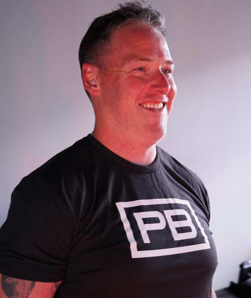 PowerBlock Fitness studio's Peter Spitsnogle, posing for a headshot wearing a black powerblock shirt.